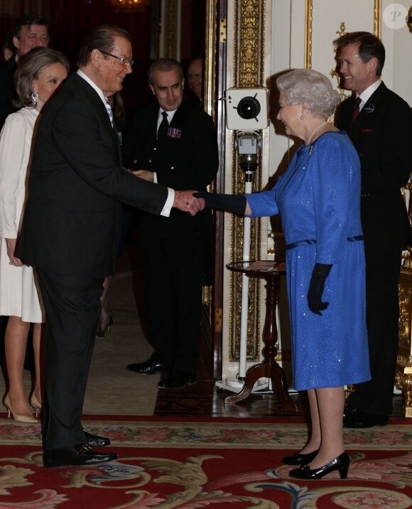 Elizabeth II salue Sir Roger Moore lors de la réception organisée le 17 février 2014 à Buckingham Palace pour célébrer les soixante ans du patronage de la Royal Academy of Dramatic Art par la reine Elizabeth II.