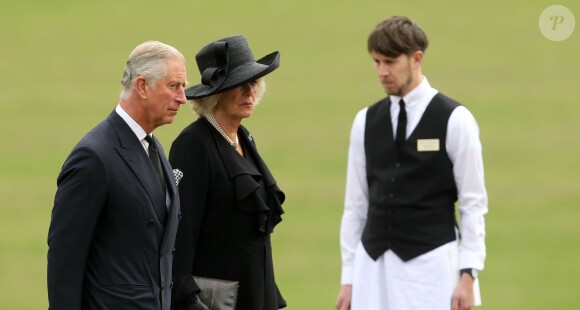 Le prince Charles et Camilla Parker Bowles devant un employé de la défunte en livrée lors des funérailles de leur amie Deborah Cavendish, née Mitford, duchesse douairière du Devonshire, le 2 octobre 2014 à Chatsworth.