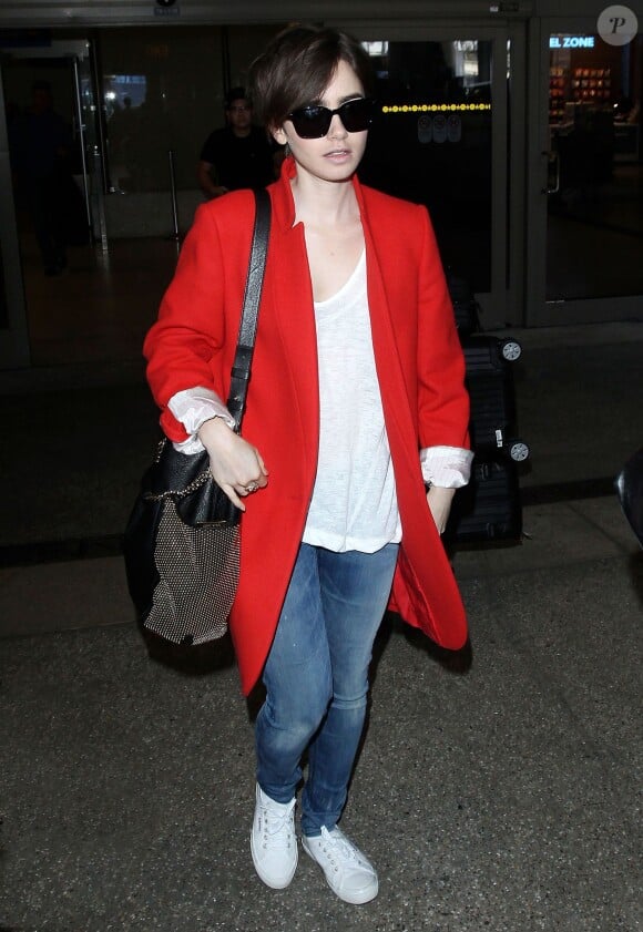 Lily Collins à l'aéroport LAX de Los Angeles, porte un manteau Stella McCartney, un sac clouté Jimmy Choo (modèle Anna) et des baskets Superga. Le 11 avril 2015.
