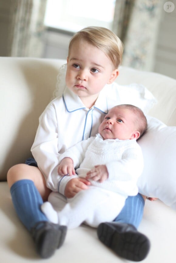 Le prince George avec sa soeur la princesse Charlotte de Cambridge sur les genoux, en mai 2015, après sa naissance, photographiés par leur maman Kate Middleton.