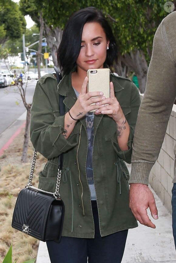 Demi Lovato à la sortie d'un immeuble accompagnée de son garde du corps à West Hollywood. Demi s'amuse à prendre les photographes en photo avec son Iphone. Le 18 mai 2016