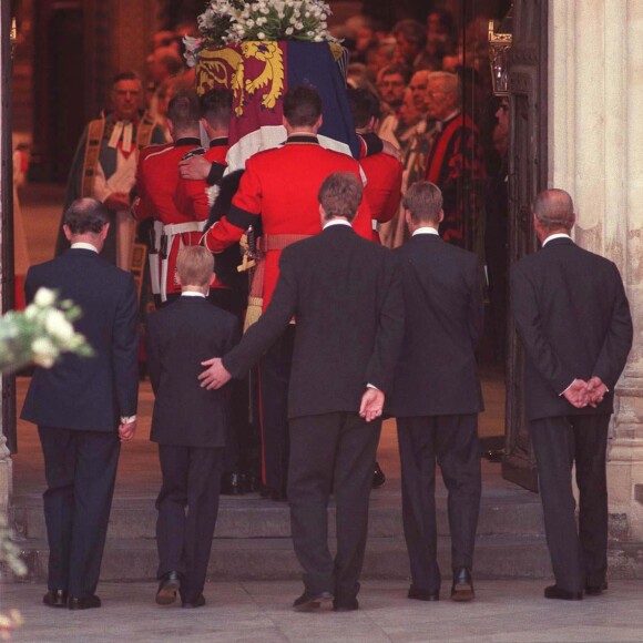 Charles Spencer passant une main réconfortante dans le dos du prince Harry à l'entrée de l'abbaye de Westminster... Le prince William et le prince Harry, alors âgés de 15 et 12 ans, ont dû marcher derrière le cercueil de leur mère la Lady Diana en public avec le duc d'Edimbourg, le prince Charles et le comte Charles Spencer, pendant une interminable demi-heure lors des obsèques nationales de la princesse le 6 septembre 1997 à Londres. "Bien sûr qu'ils ne voulaient pas faire ça", a révélé en juillet 2017 leur oncle Charles Spencer.