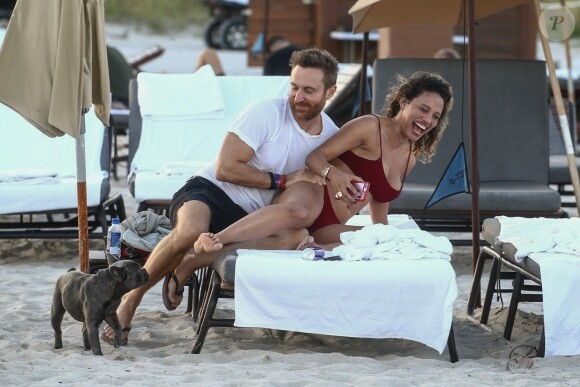 David Guetta et sa compagne Jessica Ledon, qui porte un diamant à l'annulaire gauche, passent du bon temps sur la plage en compagnie de leur petit chien. Miami, le 23 novembre 2018.