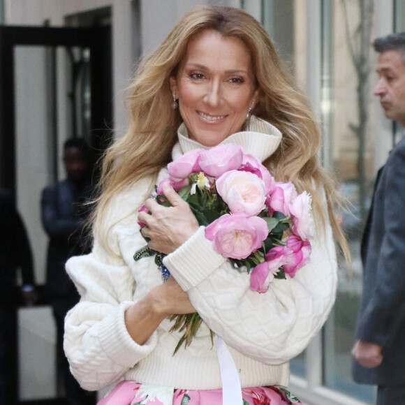 Celine Dion rayonnante et très souriante dans un ensemble pull écru et jupe bouffante fleurie salue ses fans à la sortie de son hôtel à New York, le 8 mars 2020