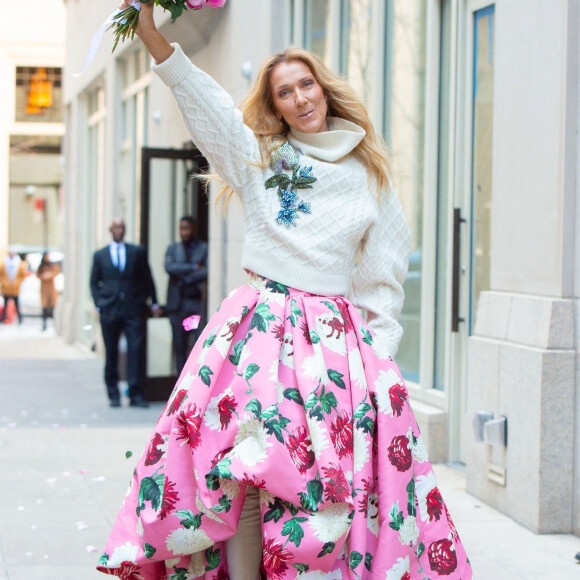 Celine Dion rayonnante et très souriante dans un ensemble pull écru et jupe bouffante fleurie salue ses fans à la sortie de son hôtel à New York, le 8 mars 2020
