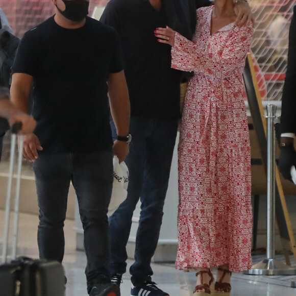 Exclusif - Laeticia Hallyday et son compagnon Pascal Balland prennent un vol à l'aéroport Roissy CDG pour une échappée à deux, sans enfants le 26 juin 2020. Le couple est resté séparé pendant le confinement lors de l'épidémie de coronavirus (COVID-19). Ils suivent les recommandations concernant le port du masque dans les transports mais ne résistent pas à échanger un baiser malgré leur barrière de tissu. 