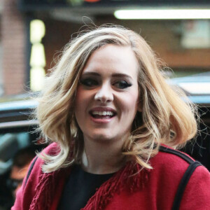 La chanteuse Adele souriante à New York le 20 novembre 2015. Elle porte un long gilet rouge à franges et continue les selfies avec ses fans.