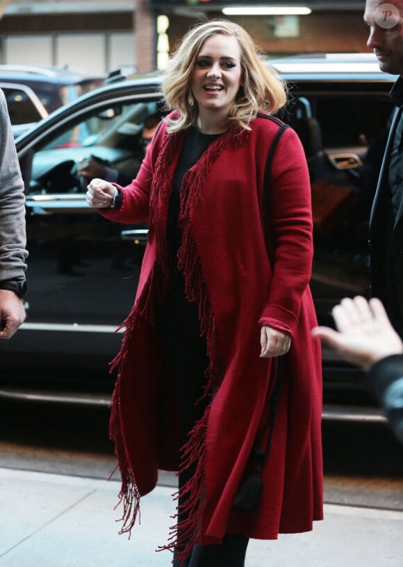 La chanteuse Adele souriante à New York le 20 novembre 2015. Elle porte un long gilet rouge à franges et continue les selfies avec ses fans.