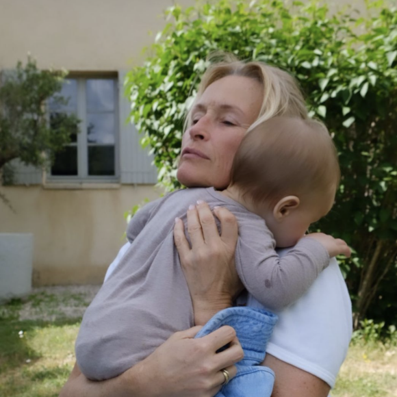 On peut ainsi voir Estelle Lefébure, au naturel, assise en tailleurs dans l'herbe avec son petit-fils dans les bras.