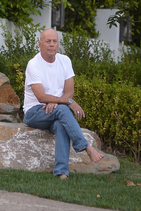 Exclusif - Bruce Willis est assis pieds nus sur un rocher et regarde passer les voitures sur Sunset Boulevard à Los Angeles, le 22 septembre 2019. Il porte un jean et un t-shirt blanc. 