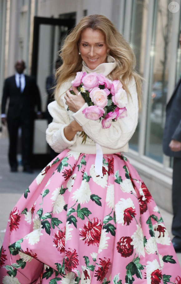 Celine Dion rayonnante et très souriante dans un ensemble pull écru et jupe bouffante fleurie salue ses fans à la sortie de son hôtel à New York, le 8 mars 2020