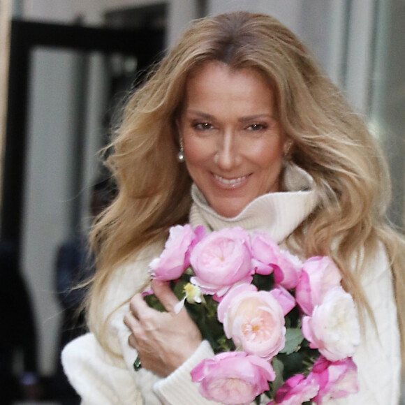 Celine Dion rayonnante et très souriante dans un ensemble pull écru et jupe bouffante fleurie salue ses fans à la sortie de son hôtel à New York, le 8 mars 2020