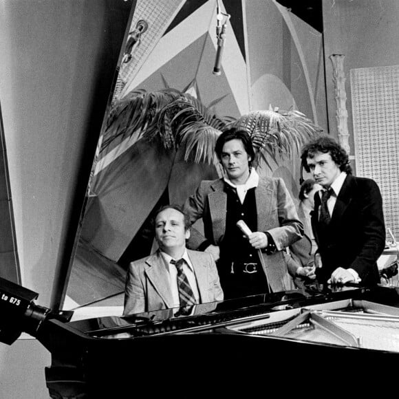 Archives - En France, à Paris, sur le plateau, de gauche à droite, Claude BOLLING, au piano, Alain DELON et Michel SARDOU, debout près du piano, en arrière-plan, Jean-Louis TRINTIGNANT. © Michel CROIZARD via Bestimage