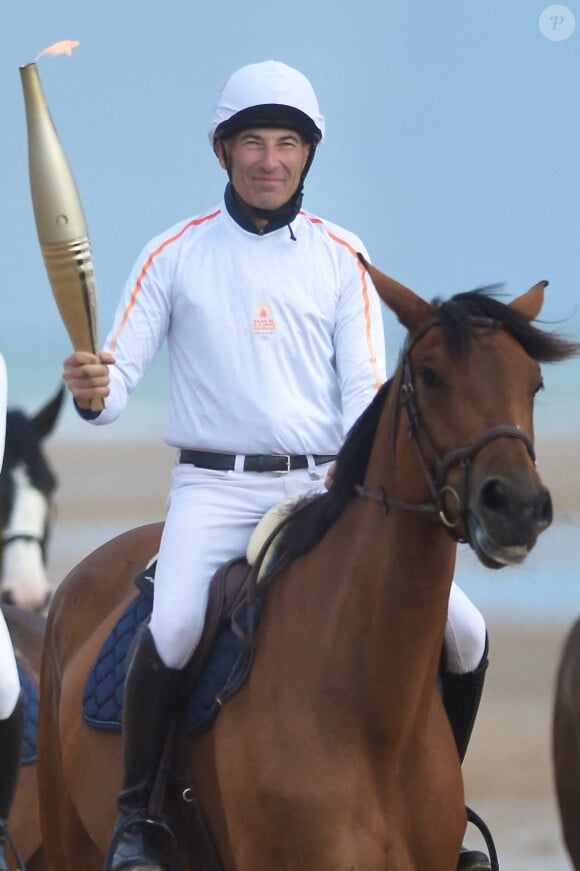 Nicolas Canteloup porte la flamme olympique à cheval, encadré par des gendarmes à cheval, lors du relais olympique de l'équipe équestre, en amont des Jeux olympiques et paralympiques de Paris 2024, sur la plage d'Omaha Beach, à Saint-Laurent-sur-mer, dans le nord-ouest de la France, le 30 mai 2024. Photo par Franck Castel/ABACAPRESS.COM