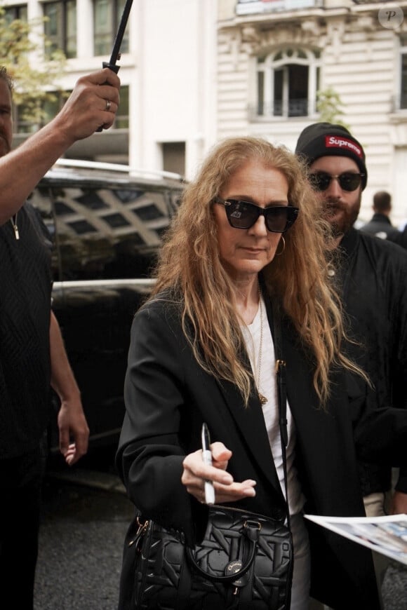 Paris, France - La chanteuse canadienne Céline Dion quitte son hôtel pour se rendre à l'aéroport, prenant le temps de saluer et de signer des autographes à la foule de fans qui l'attendent, montrant ainsi sa reconnaissance pour leur soutien.