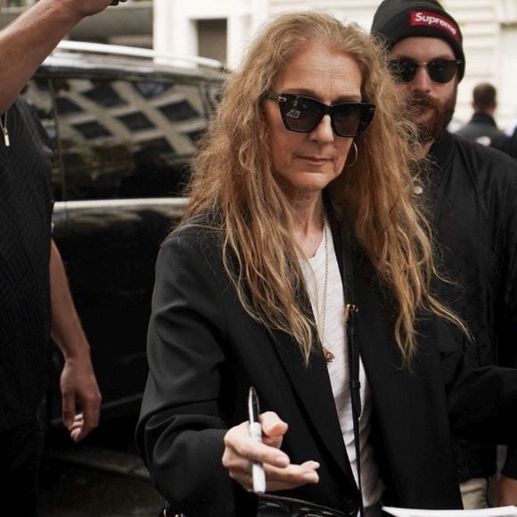 Paris, France - La chanteuse canadienne Céline Dion quitte son hôtel pour se rendre à l'aéroport, prenant le temps de saluer et de signer des autographes à la foule de fans qui l'attendent, montrant ainsi sa reconnaissance pour leur soutien.