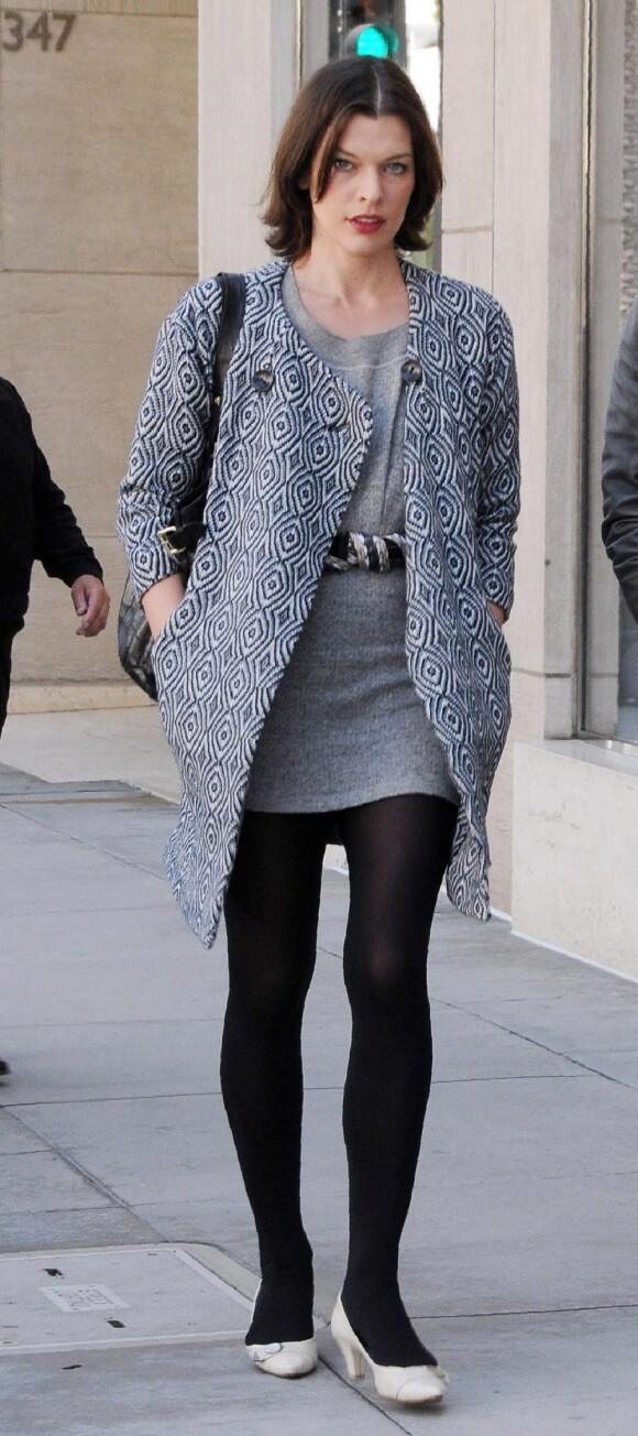 Ballerines aux pieds, collants opaques, robe en laine grise ceinturée, et manteau psyché assorti,le top model Milla Jovovich est à tomber.