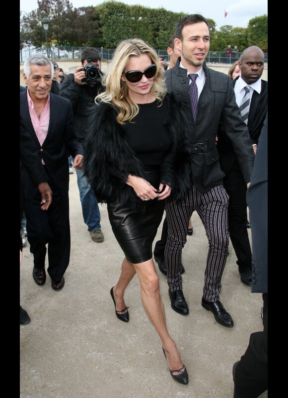 Kate Moss en total look black pour le défilé Dior. Jupe en cuir droite, escarpins pointus, lunettes XXL, le look de star hollywoodienne est assuré.