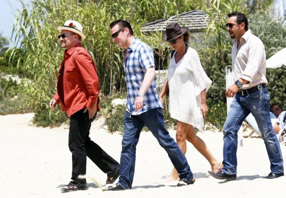 Le chanteur Bono, sa femme Alison Hewson (en robe rouge) et Larry Mullen (batteur du groupe U2, chemise bleue à carreaux) arrivent au Club 55, plage de Pampelonne à Ramatuelle, le 04 juillet 2013.