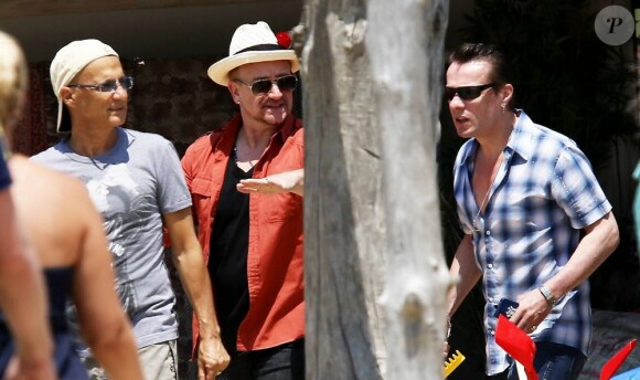 Le chanteur Bono, sa femme Alison Hewson (en robe rouge) et Larry Mullen (batteur du groupe U2, chemise bleue à carreaux) arrivent au Club 55, plage de Pampelonne à Ramatuelle, le 04 juillet 2013.