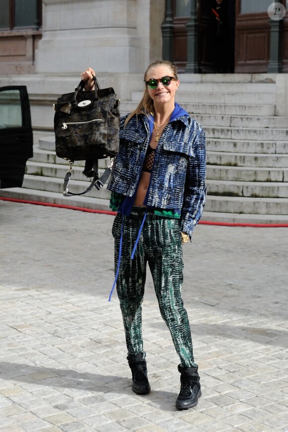 Cara Delevingne quitte l'Opéra Garnier à l'issue du défilé Stella McCartney. Elle porte une veste et un pantalon Stella McCartney, un sac de sa collection pour Mulberry et des baskets Chanel. Paris, le 3 mars 2014.