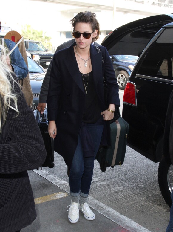 Kristen Stewart prend un vol à l'aéroport de Los Angeles avec sa présumée compagne Alicia Cargile, habillée d'un long manteau marine, d'un jean et de baskets Vans. Un sac Chanel et des lunettes de soleil accessoirisent sa tenue. Le 4 février 2015.
