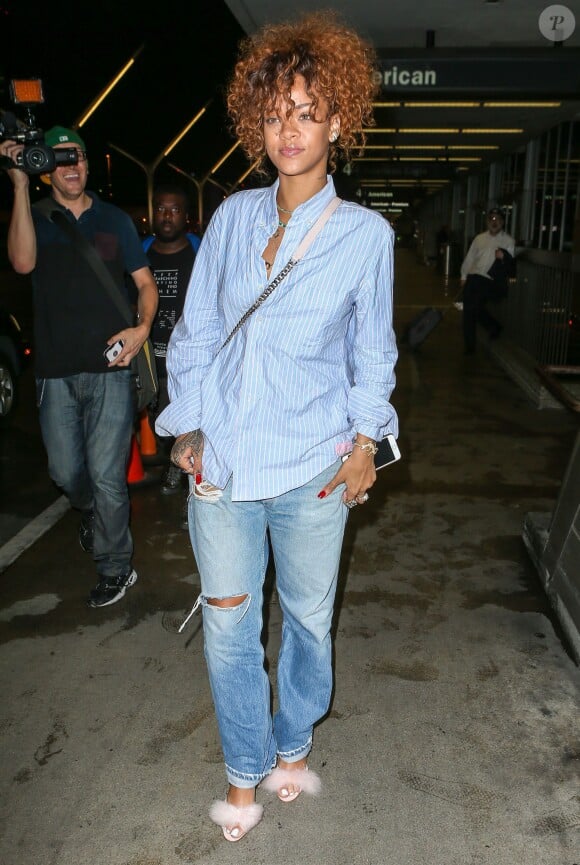 Rihanna arrive à l'aéroport LAX à Los Angeles, habillée d'une chemise rayée, d'un jean coupe boyfriend et de ses sandales rose pâle. La chanteuse de 27 ans porte en bandoulière un sac Christian Dior (modèle Diorama) blanc. Le 21 juillet 2015.