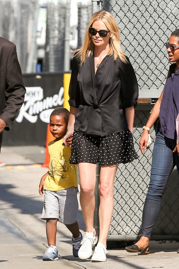 Charlize Theron arrive sur le plateau de l'émission "Jimmy Kimmel Live!" avec son fils Jackson à Hollywood, habillée d'une veste kimono noire, d'une jupe à poids et de baskets Isabel Marant Étoile (modèle Bart). Le 20 juillet 2015.