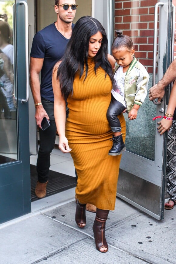 Kim Kardashian, enceinte et avec sa fille North West (2 ans), quitte l'appartement de Kanye West habillée d'une robe jaune miel Laquan Smith (collection automne 2015) et de bottes marrons Givenchy (collection printemps-été 2015). New York, le 9 septembre 2015.
