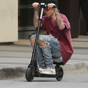 Justin Bieber fait de la trottinette devant son hôtel à Hollywood. Il porte des lunettes de vue rondes le 24 novembre 2015