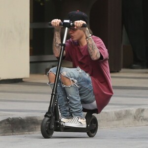 Justin Bieber fait de la trottinette devant son hôtel à Hollywood. Il porte des lunettes de vue rondes le 24 novembre 2015