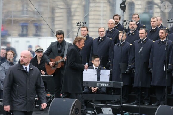 Johnny Hallyday, accompagné par Yodelice et Yarol Poupaud, chante "Un dimanche de janvier" en hommage aux victimes des attentats de janvier et novembre. Place de la République à Paris, le 10 janvier 2016.