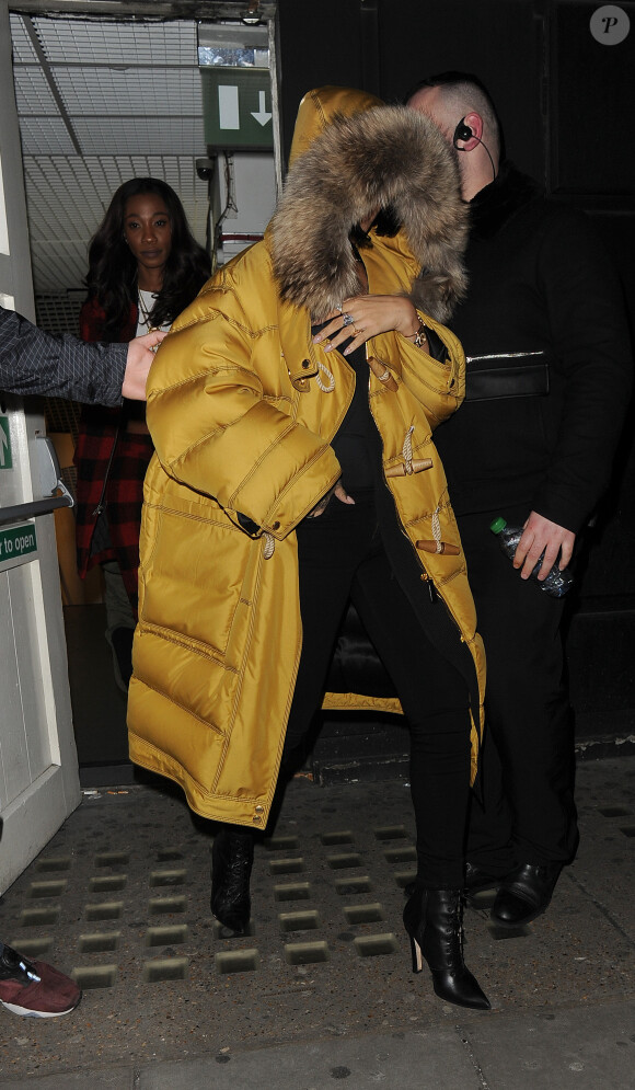 Rihanna quitte le Libertine à Londres, habillée de son manteau Burberry, d'un top et d'un jean noirs, et de bottines Manolo Blahnik. Le 23 février 2016.