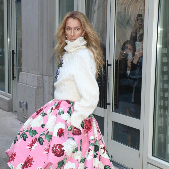 Celine Dion rayonnante et très souriante dans un ensemble pull écru et jupe bouffante fleurie salue ses fans à la sortie de son hôtel à New York, le 8 mars 2020 