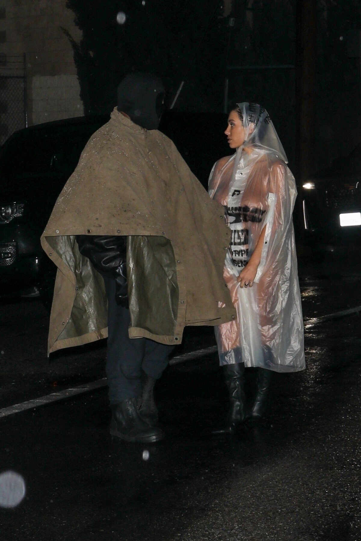 Photo : Exclusif - Kanye West, portant un masque intégral et un poncho,  avec sa femme Bianca Censori, nue en imperméable transparent, arrivent à un  studio à Los Angeles, le 5 février 2024. - Purepeople