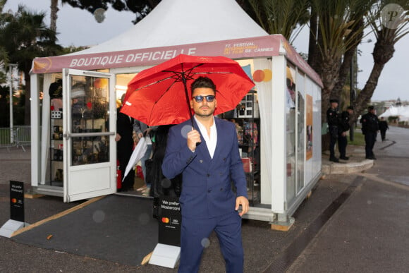 Kev Adams brave la pluie avec un parapluie rouge lors de la première journée du 77ème Festival de Cannes au Palais des Festivals à Cannes, France, le 14 mai 2024, dans le cadre du programme Photo by Cyril CHATEAU/ABACAPRESS.COM
