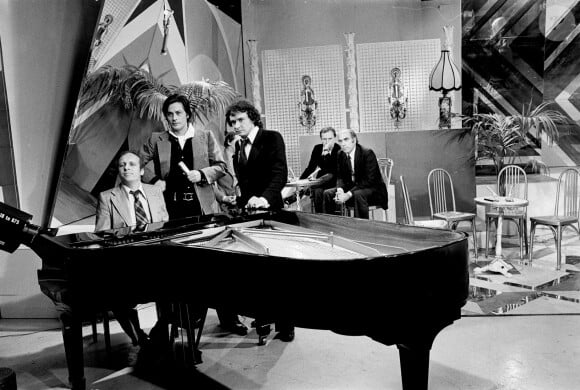 Archives - En France, à Paris, sur le plateau, de gauche à droite, Claude BOLLING, au piano, Alain DELON et Michel SARDOU, debout près du piano, en arrière-plan, Jean-Louis TRINTIGNANT. © Michel CROIZARD via Bestimage