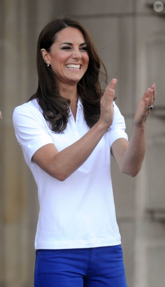 Kate Middleton, vêtue du T-Shirt officiel de la délégation olympique britannique, lors du passage du relais de la flamme olympique à Buckingham Palace, le 26 juillet 2012, à l'avant-dernier jour du périple. Avec William et Harry, elle a applaudi le relais entre Wai-Ming et John Hulse.