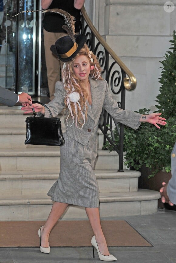 Lady Gaga, vêtue d'un tailleur gris Vivienne Westwood, quitte l'hôtel Langham à Londres et assure le show devant ses fans. Le 28 août 2013.