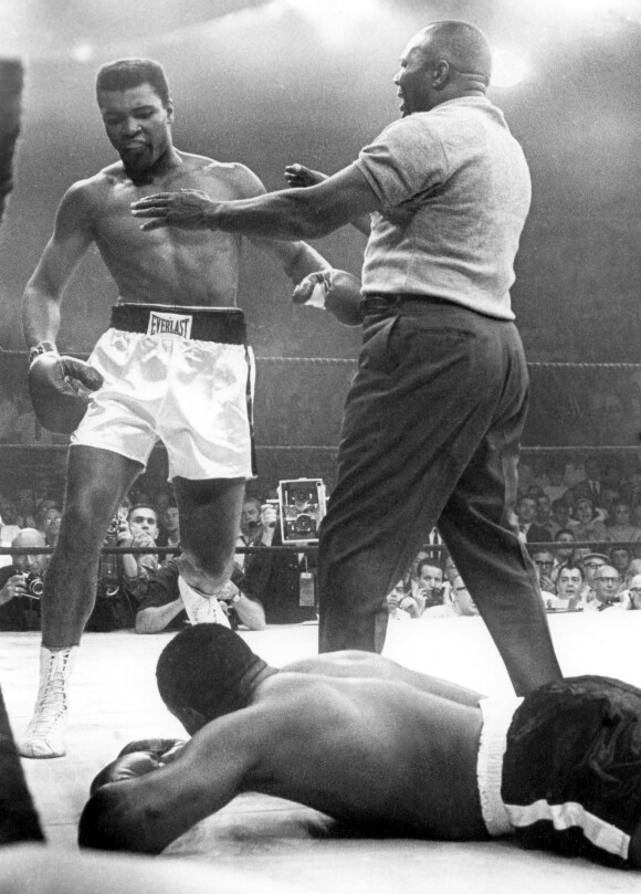 Cassius Clay, aka Mohamed Ali, vient de mettre au tapis Sonny Liston lors de leur combat du 25 mai 1965 à Lewiston. Un combat sur lequel pèse de forts soupçons, comme la première rencontre entre les deux boxeurs du 25 février 1964 pour lequel Sonny Liston aurait touché un million de dollars pour se coucher