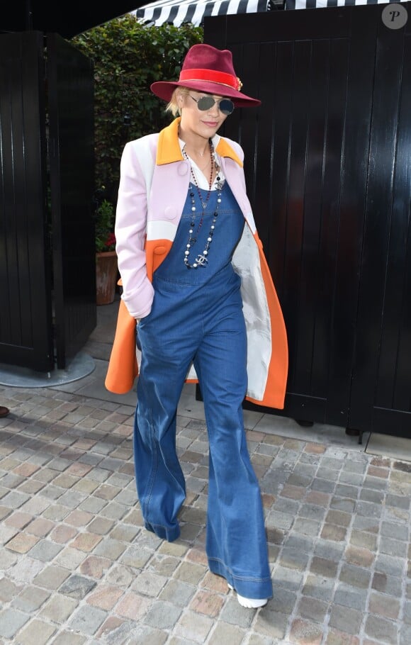 Rita Ora à Londres, porte un manteau Prada, une salopette et des chaussures Stella McCartney, un chemisier blanc et un sautoir Chanel. Le 20 octobre 2014.