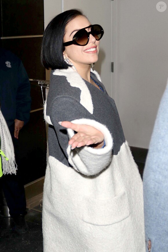 Lady Gaga arrive en souriant et adresse un baiser de la main aux photographes, à JFK New York le 17 février 2015.  