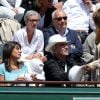 Raymond Domenech et sa compagne Estelle Denis dans les tribunes des Internationaux de France de tennis de Roland-Garros à Paris, le 1er juin 2015.