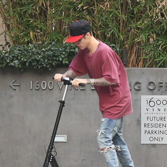 Justin Bieber fait de la trottinette devant son hôtel à Hollywood. Il porte des lunettes de vue rondes le 24 novembre 2015