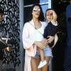 Kourtney Kardashian porte sa fille Penelope Disick à Miami, habillée d'un gilet couleur chair, d'un body blanc, d'un mini-short en jean Levi's et de sandales Stuart Weitzman. Des lunettes de soleil Victoria Beckham et un sac Givenchy (modèle Pandora Box) accessoirisent sa tenue. Le 24 avril 2016.
