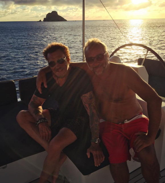 En balade en voilier, Laeticia prend en photo Johnny Hallyday et l'acteur Antoine Duléry devant le soleil couchant. À Saint-Barthélemy, fin août 2016.