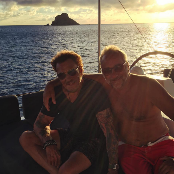 En balade en voilier, Laeticia prend en photo Johnny Hallyday et l'acteur Antoine Duléry devant le soleil couchant. À Saint-Barthélemy, fin août 2016.