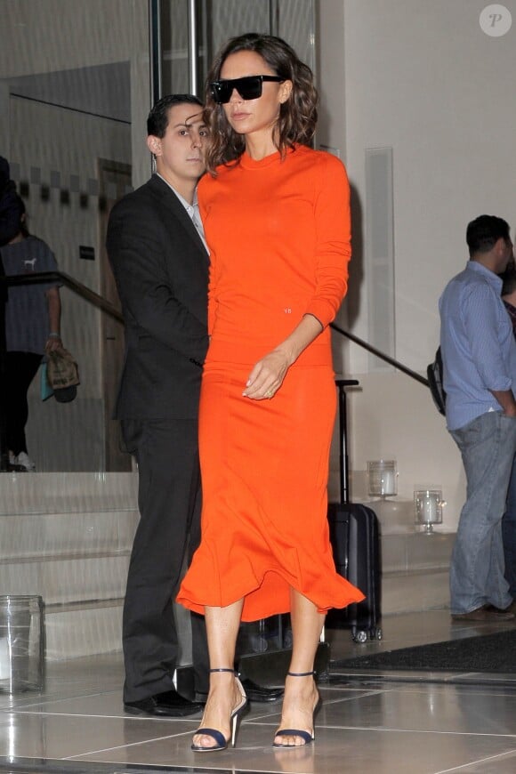 Victoria Beckham quitte l'EDITION New York à New York, habillée d'un pull et d'une jupe oranges Victoria Beckham. Des lunettes Victoria Beckham et des sandales Manolo Blahnik complètent sa tenue. Le 12 septembre 2016.