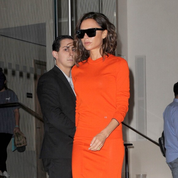 Victoria Beckham quitte l'EDITION New York à New York, habillée d'un pull et d'une jupe oranges Victoria Beckham. Des lunettes Victoria Beckham et des sandales Manolo Blahnik complètent sa tenue. Le 12 septembre 2016.