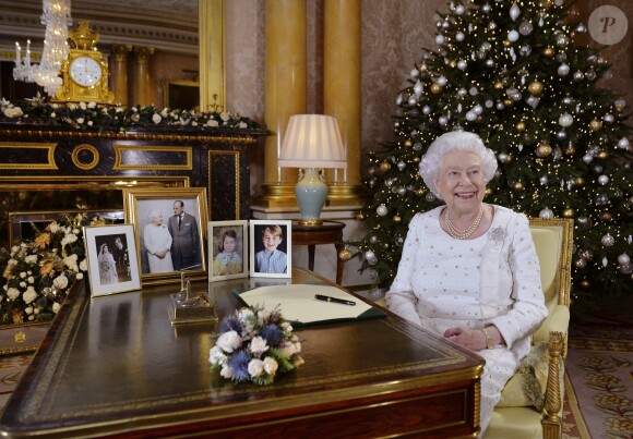 La reine Elizabeth II dans le salon 1844 au palais de Buckingham pour l'enregistrement de son allocution de Noël, le 25 décembre 2017. Sur le bureau à côté d'elle, des photos de George et Charlotte de Cambridge, de son mariage avec le prince Philip et de leurs noces de platine. Mais dans la pièce figurait aussi une photo des fiançailles du prince Harry et de Meghan Markle, qui s'apprête à entrer dans la famille.